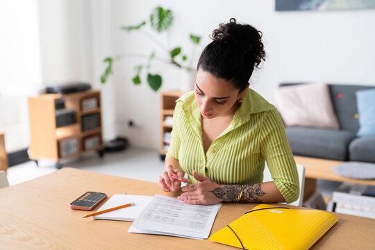 A woman with a thoughtful expression fills out paperwork, attention to detail in a modern home setting