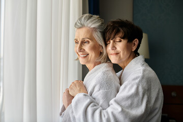 Senior lesbian couple embrace warmly in a hotel room.