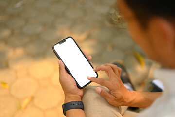 Young businessman holding smartphone with white empty screen sitting outdoor. Close up shot