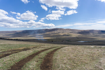 View of the mountains and a small lake in the valley. Tire tracks are visible on the grass