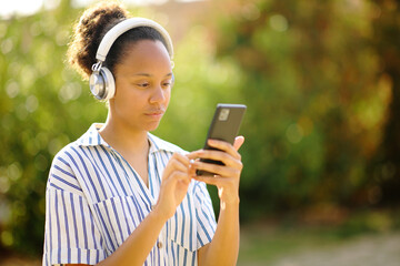 Black woman wearing headphone using phone in a garden