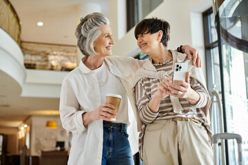 Two women, a senior lesbian couple, standing side by side holding coffee cups.