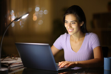 Happy woman at home using a laptop in the night