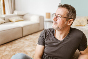 Pensive middle-aged man sitting on living room floor