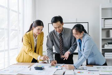Strategic Planning in Session: A team of Asian business professionals huddle over spreadsheets and charts, their focused expressions reflecting the intensity of their collaborative analysis. 