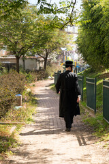 Religious jew in a black frock coat and black hat walks through a green park (179)