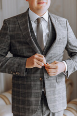 A man in a suit is getting ready to go out. He is wearing a plaid jacket and a tie