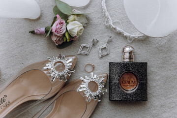A pair of high heels, a bottle of perfume, and a flower are displayed on a table