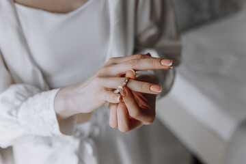 A woman is holding a ring in her hand. She is wearing a white gown and has her hands clasped...