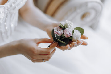 A woman is holding a boutonniere in her hand. The boutonniere is made of pink flowers and is placed...
