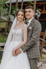 Fototapeta premium A bride and groom are posing for a picture in front of a wooden staircase. The bride is wearing a white dress and the groom is wearing a suit. Scene is happy and celebratory