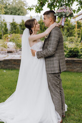A bride and groom are standing in a grassy area, with the bride wearing a white dress and the groom wearing a suit