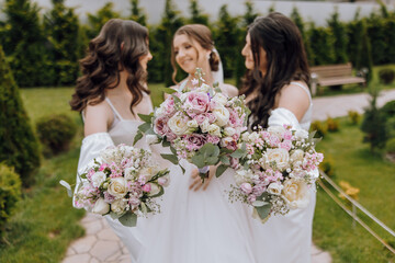 Three women are holding bouquets of flowers and posing for a picture. Scene is joyful and celebratory, as the women are likely attending a wedding or other special event