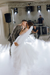 A bride and groom are kissing in the air at a wedding. The bride is wearing a white dress and the groom is wearing a suit. The scene is lively and joyful, with the couple dancing