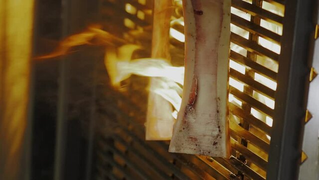The process of cooking bone marrow on a grill over an open fire. Chef cooking on grill, close up, vertical video