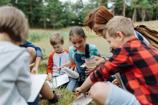 Young students analyzing water quality, ph level with indicator strips during biology field teaching class. Female teacher during outdoor active education.
