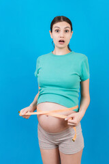 pregnant woman measuring her growing tummy with a tape measure at colored background. Check a baby development. Copy space