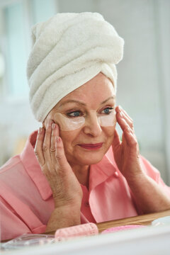 Smiling senior woman applying under eye patches at home