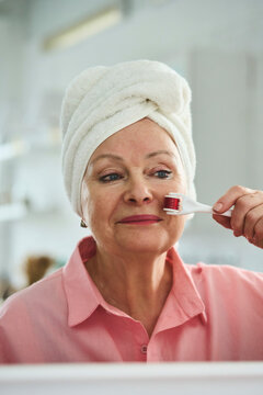 Senior woman using dermaroller on face at home