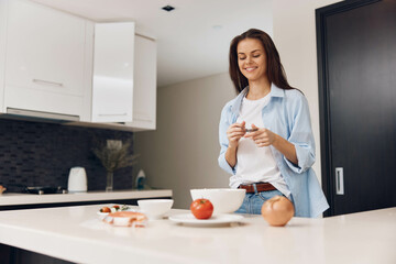 Woman standing in kitchen with bowl of fruit and cereal, healthy breakfast concept with fresh ingredients on table