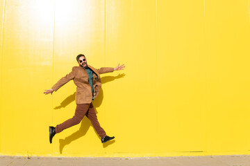 Cheerful man jumping in front of yellow wall