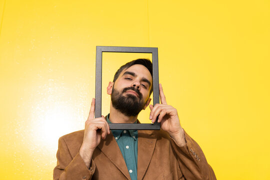 Man wearing brown jacket and looking through photo frame