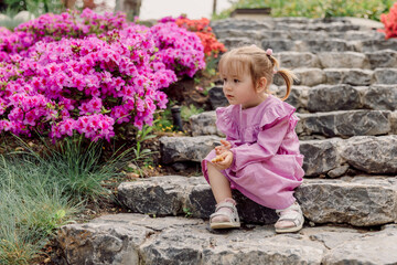 Cute child girl sitting on the steps outdoor in summer park. Cute girl and pink flowers