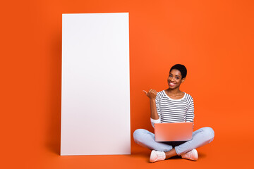 Portrait of attractive cheerful girl using laptop demonstrating copy space ad look isolated over vibrant orange color background