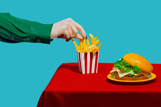 Hand of woman picking up french fries from table against blue background