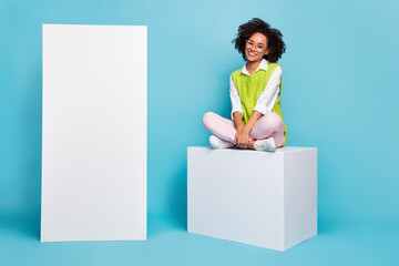 Photo of charming brown haired lady sit cube podium next to advertisement placard isolated on blue...