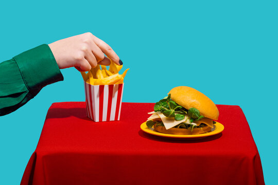 Woman reaching for french fries near cheeseburger on table against blue background