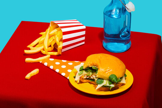 Chicken burger and french fries with soda bottle on table against blue background