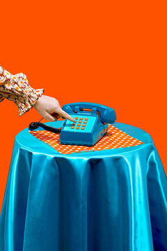 Hand of woman dialing on keypad of telephone against orange background