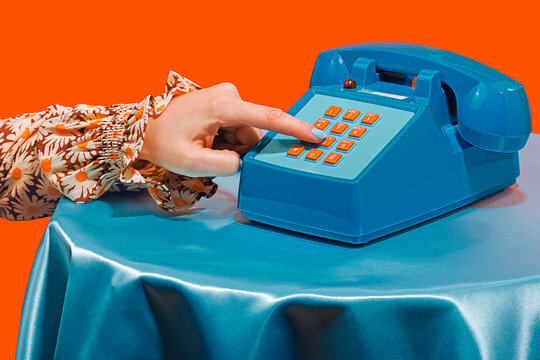 Woman dialing number on telephone against orange background