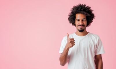 Young modern African American man looking directly towards the camera, with a two thumbs up gesture standing isolated on light pink background.