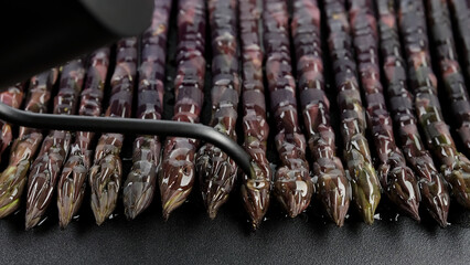 Chef pouring oil on fresh purple asparagus bunch before cooking