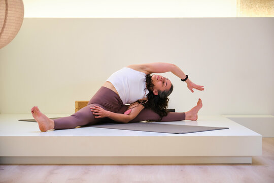 A woman is doing a yoga pose, parsva upavistha konasana, on a mat. She is in a split position and is looking at a side.