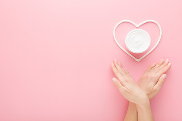 Young adult woman hands and white heart shape with cream jar on pastel pink table background. Care about clean and soft body skin. Closeup. Point of view shot. Empty place for text. Top down view. - 800102318