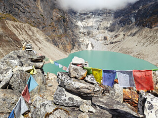 A turquoise glacial lake nestled in the Himalayan mountains of Nepal, with cloudy skies above
