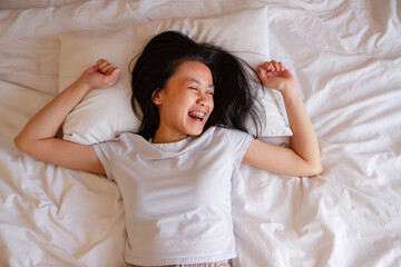 Top view of happy asian young woman lying in bed