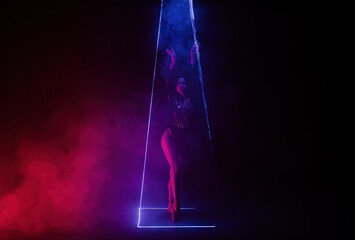 Ballet dancer in pointe under multicolor neon laser light on stage. Woman ballerina posing in dark...