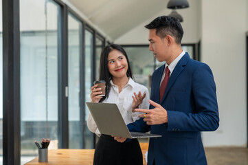 Focused businesswoman holding a laptop while discussing with a colleague, highlighting teamwork and digital workflow in a modern office.