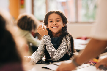 Happy little girl sitting in class, young student enjoying elementary school
