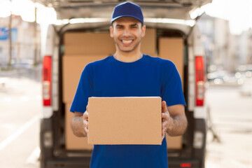 Cheerful man carrying package from delivery car, holding cardboard box and smiling. Courier service...