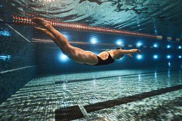 girl swimmer swims in the pool in a dark swimsuit and swimming goggles at a competition. underwater...