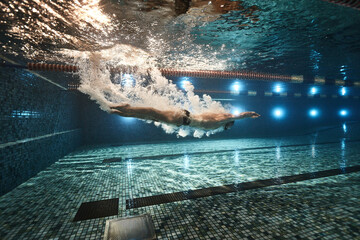 guy athlete swimmer jumps into the water in the pool and swims through air bubbles underwater...