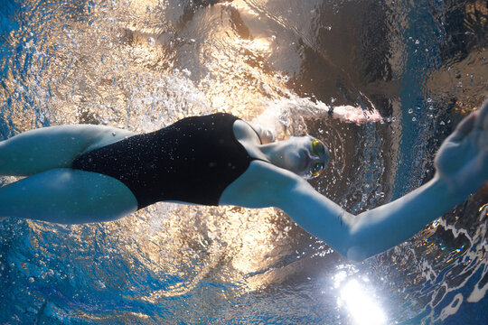 girl swimmer swims in the pool in a dark swimsuit and swimming goggles at a competition. underwater view. underwater advertising photography for swimming lessons