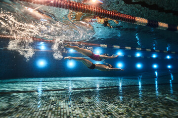 beautiful athletes swimmers guy and girl synchronously swim underwater in the pool on top of each other in dolphin style