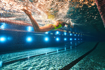 a beautiful young athletic girl in a yellow swimsuit and swimming goggles swims in a sports pool....