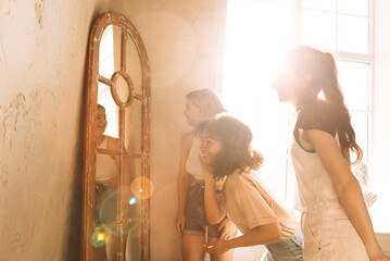 Three charming mixed-race teenagers apply makeup in front of a mirror.